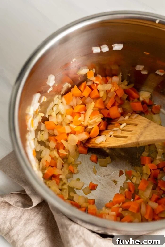 Diced onion, garlic, and carrots are being sautéed in an Instant Pot with a wooden spoon, creating a fragrant and softened base for the pilaf.