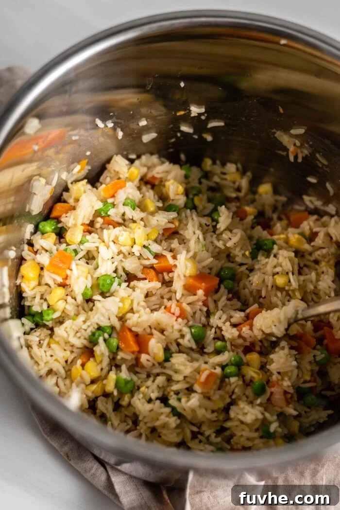 A close-up of the cooked vegetable rice pilaf inside an Instant Pot, showing fluffy basmati rice mixed with bright green peas and yellow corn kernels, ready to be fluffed.