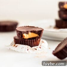 Stack of 2 chocolate peanut butter cups, one has a bit out of it to show inside. More cups in background.