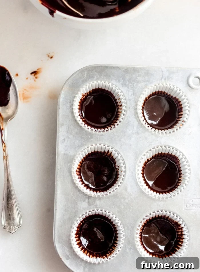 Chocolate mixture carefully spooned into a muffin tin lined with paper liners, with a spoon resting nearby.