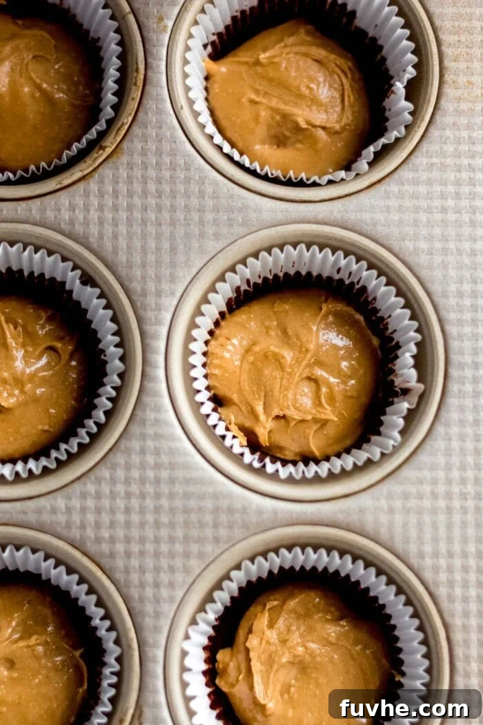 Overhead view of peanut butter filling evenly spooned into a lined muffin tin, ready for the final chocolate layer.