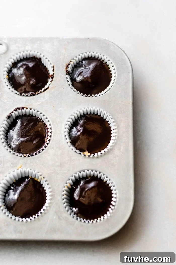Chocolate-filled cups in a lined muffin tin, with the final layer of chocolate settling beautifully.