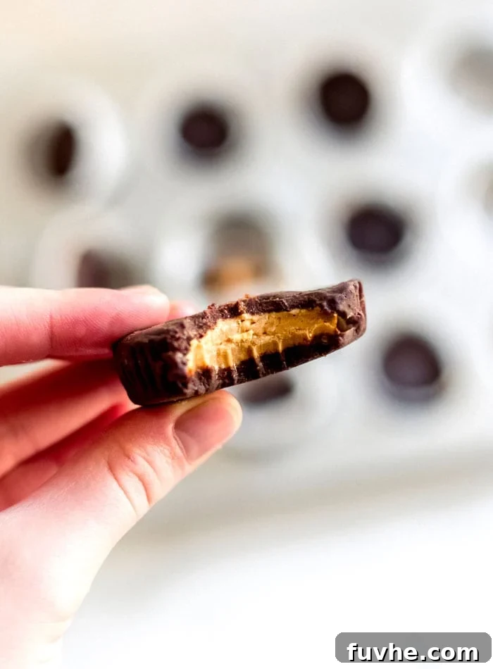 A hand holding a perfectly formed vegan chocolate peanut butter cup, with a bite taken out to reveal the creamy filling.