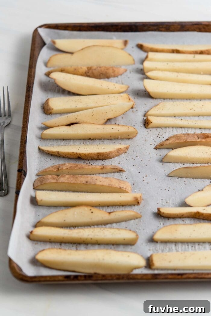 Sliced potato wedges spread evenly on a parchment-lined baking tray, ready for roasting.