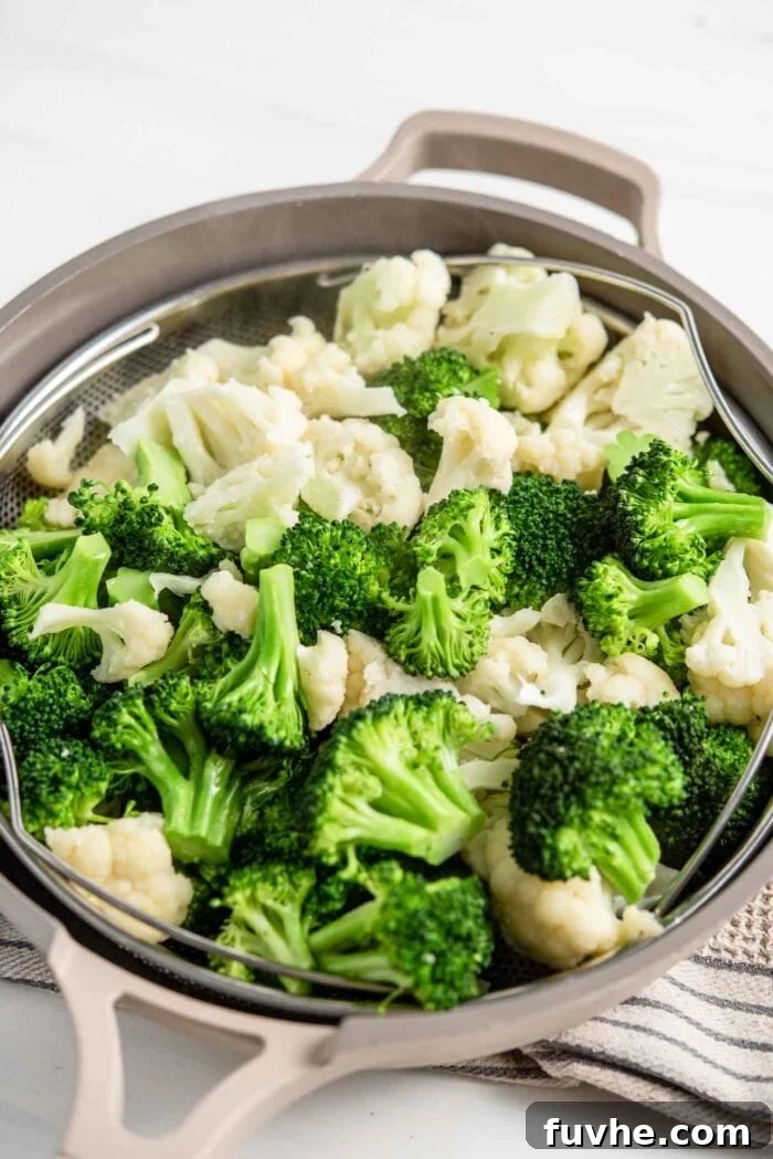 Freshly chopped broccoli and cauliflower florets neatly arranged in a steamer basket, ready for steaming.