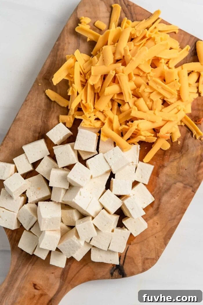 Cubed tofu and a pile of grated vegan cheese on a cutting board, ready to be added to the bowls.