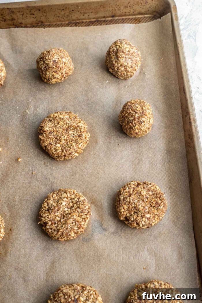 Small cookies made from chopped almonds and dates on a baking tray lined with parchment paper.