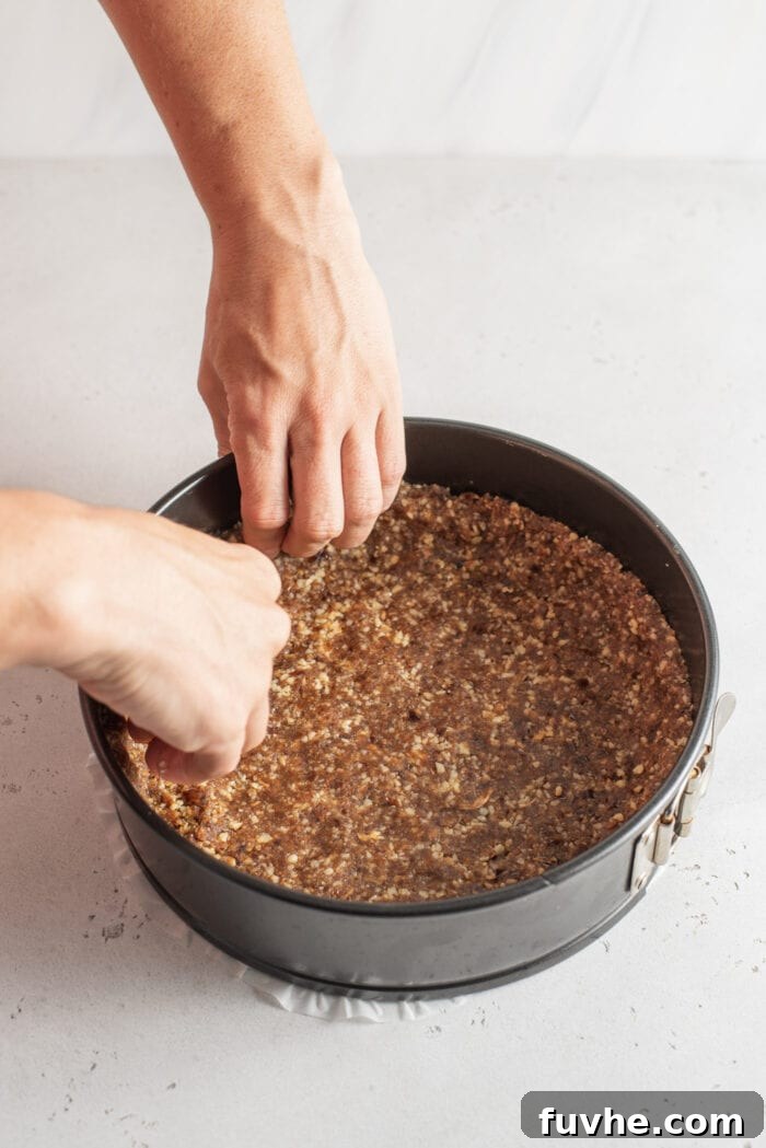 Easy Vegan No-Bake Pumpkin Cheesecake 5 Hands meticulously pressing the date and walnut crust mixture into an 8-9 inch springform pan, creating a firm base and sides.