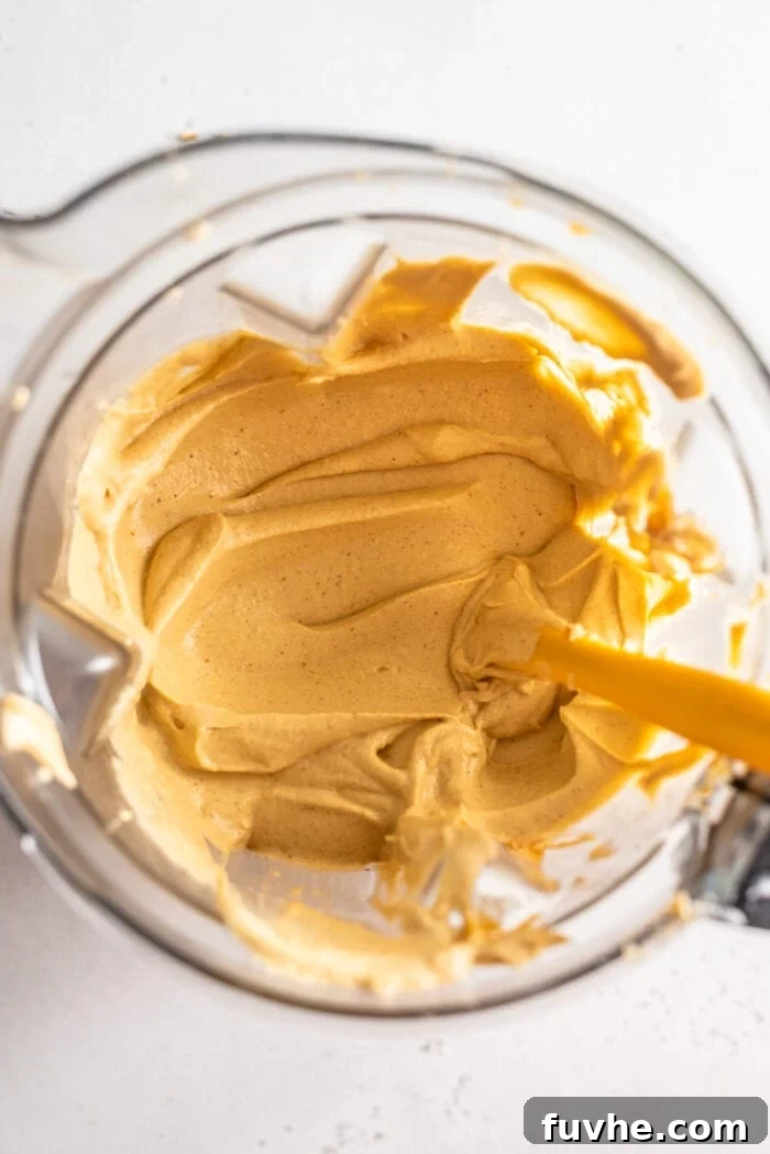 Easy Vegan No-Bake Pumpkin Cheesecake 6 A smooth, creamy, orange-hued pumpkin cheesecake filling in a high-speed blender, with a spatula resting inside.