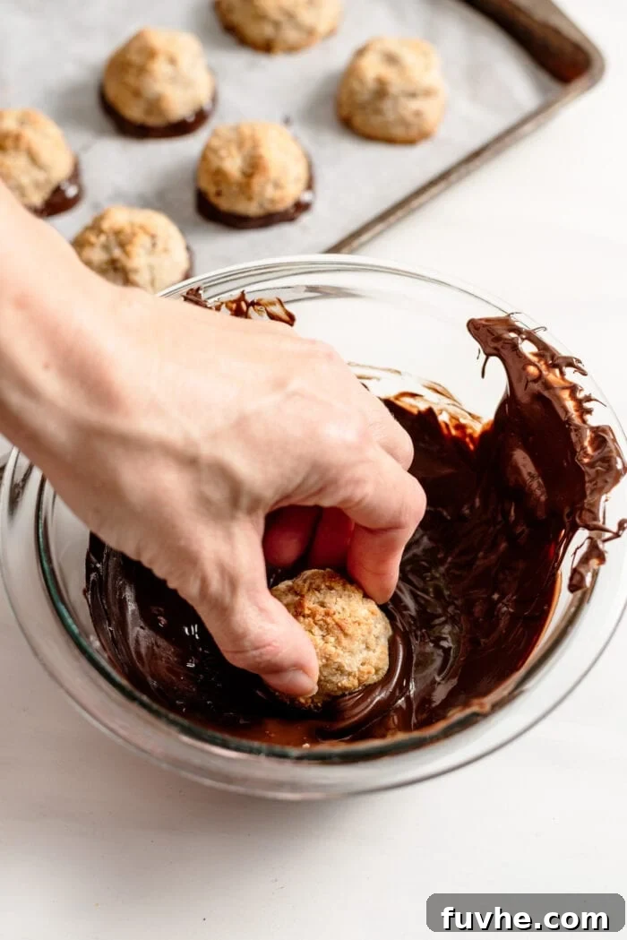 Hand dipping a coconut macaroon into a bowl of melted chocolate.