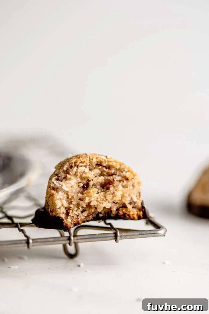 A chocolate-dipped coconut macaroon with a bite taken out of it sitting on a cooling rack.
