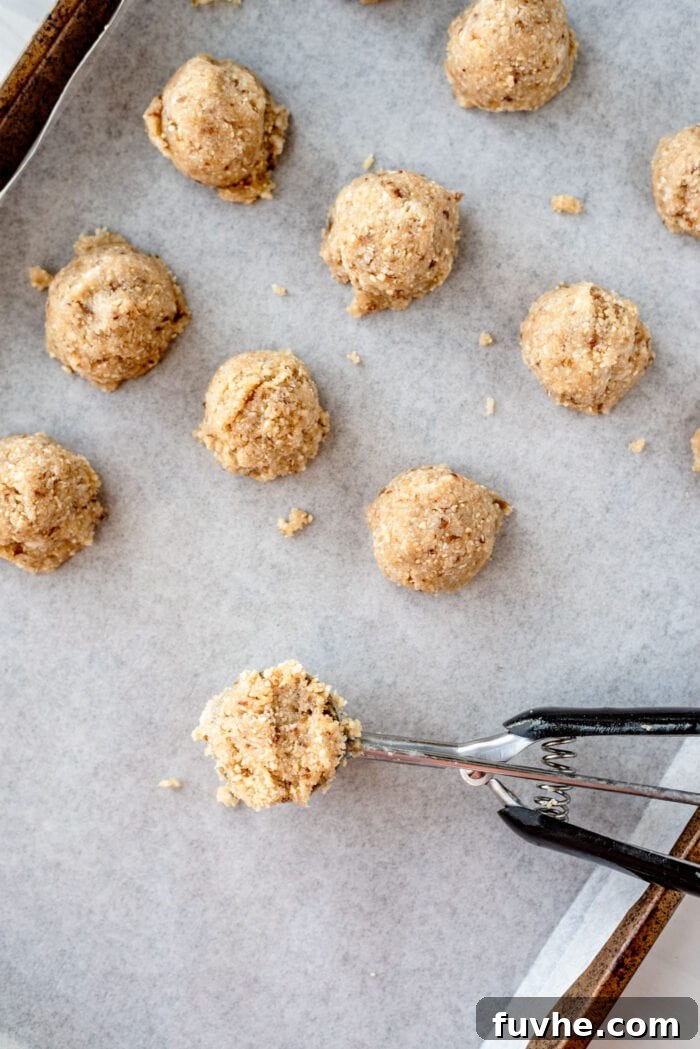 Ice cream scoop with macaroon dough in it on a baking tray of macaroons.