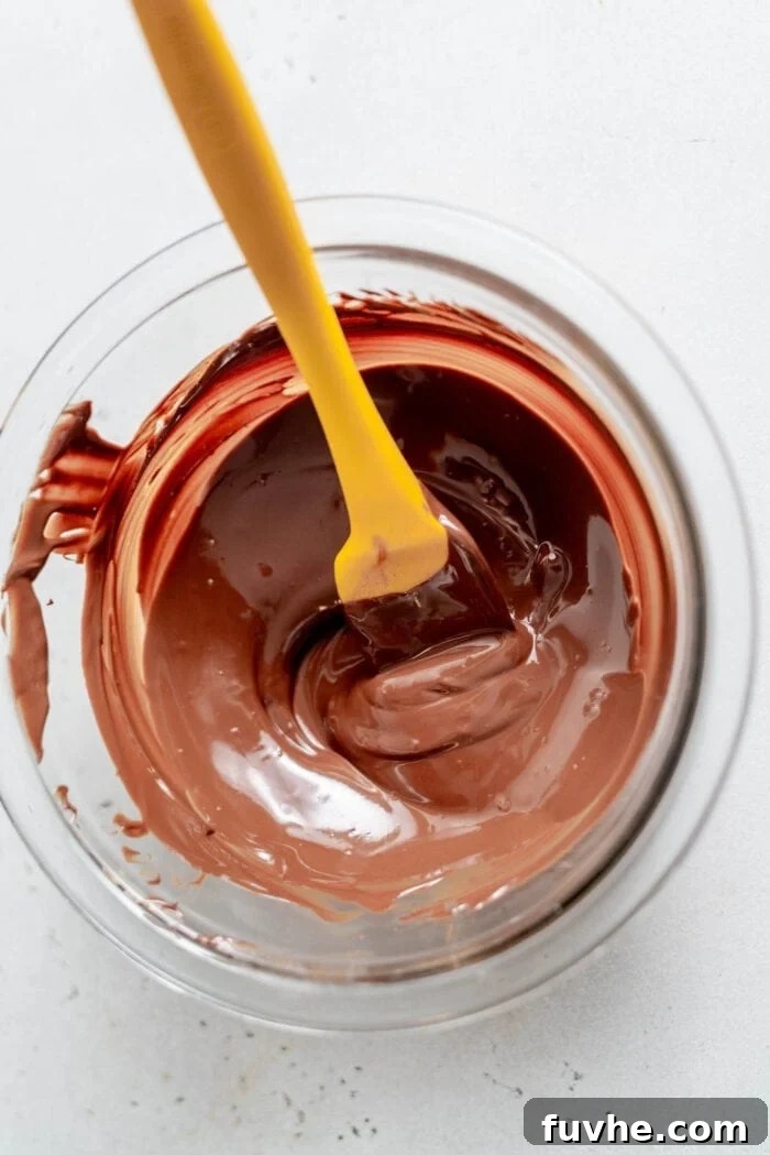 Melted chocolate in a glass mixing bowl with a spatula.
