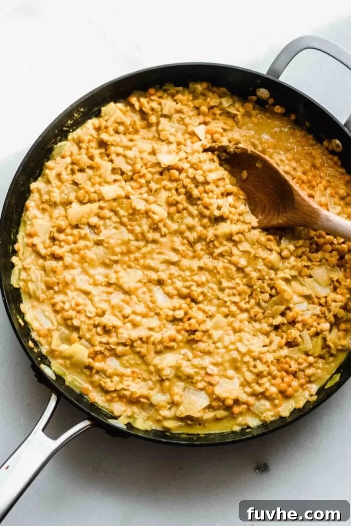 Creamy Vegan Coconut Red Lentil Dahl 6 A creamy, thick red lentil dahl simmering gently in a skillet, indicating it's almost ready.