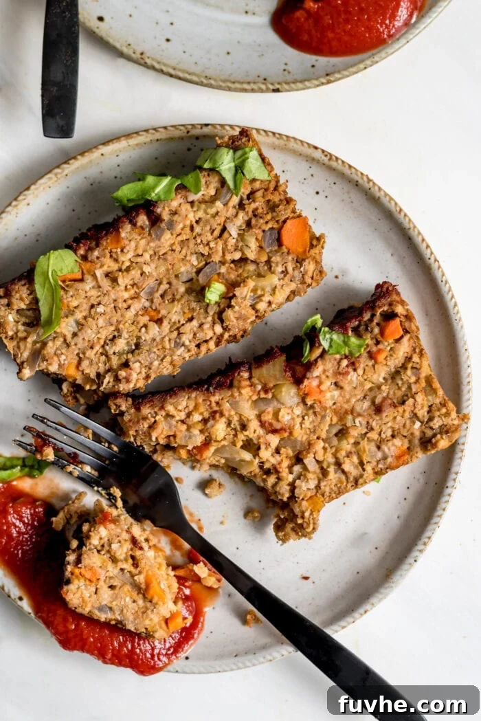 Two perfectly sliced portions of vegan chickpea meatloaf, served on a small plate with a side of tangy ketchup, ready to be enjoyed. A fork rests beside it, inviting a delicious meal.