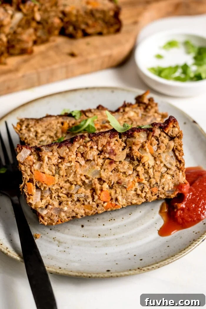 Two enticing slices of vegetarian chickpea meatloaf, perfectly browned and textured, served on a white plate alongside a dollop of vibrant ketchup. A fork stands ready on the plate.