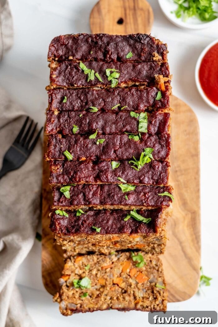 An overhead view of a vegetarian meatloaf, expertly cut into thick slices on a rustic wooden cutting board. One slice is laid flat, revealing the delicious, textured interior of the loaf.