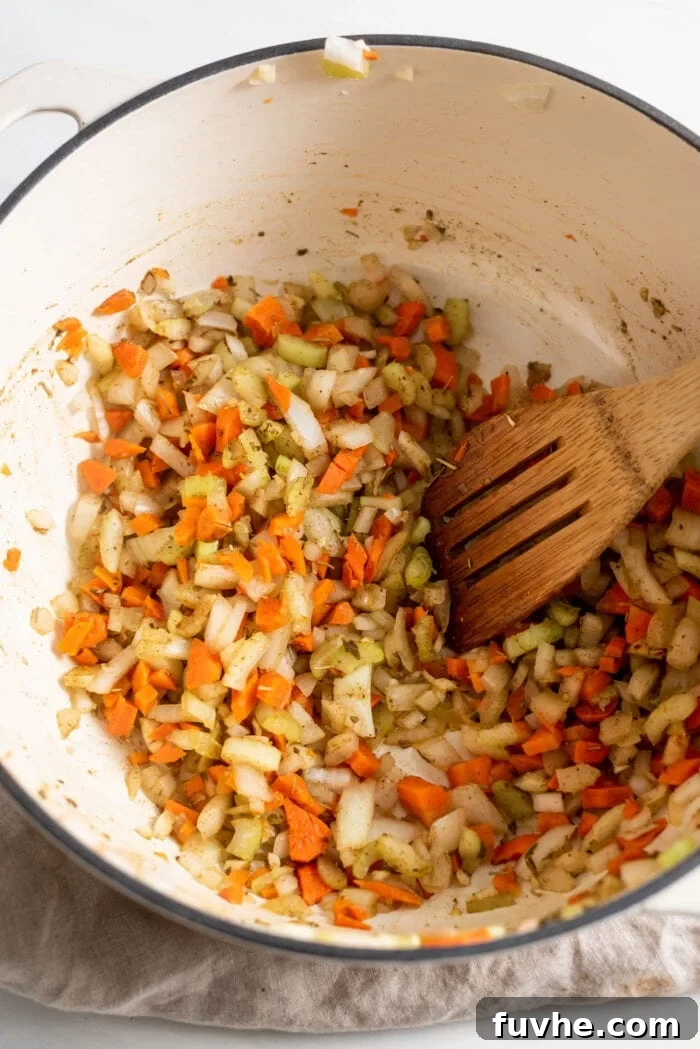 A vibrant mix of diced carrots, onions, celery, and garlic, along with fragrant dried herbs, gently cooking in a large soup pot on the stovetop.