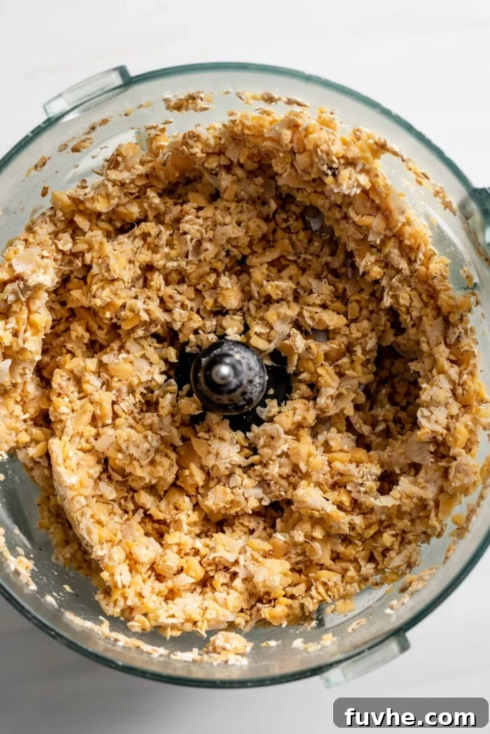 Drained chickpeas are blended into a robust, chunky mixture within a food processor, providing the perfect 'meaty' texture for the vegan loaf.