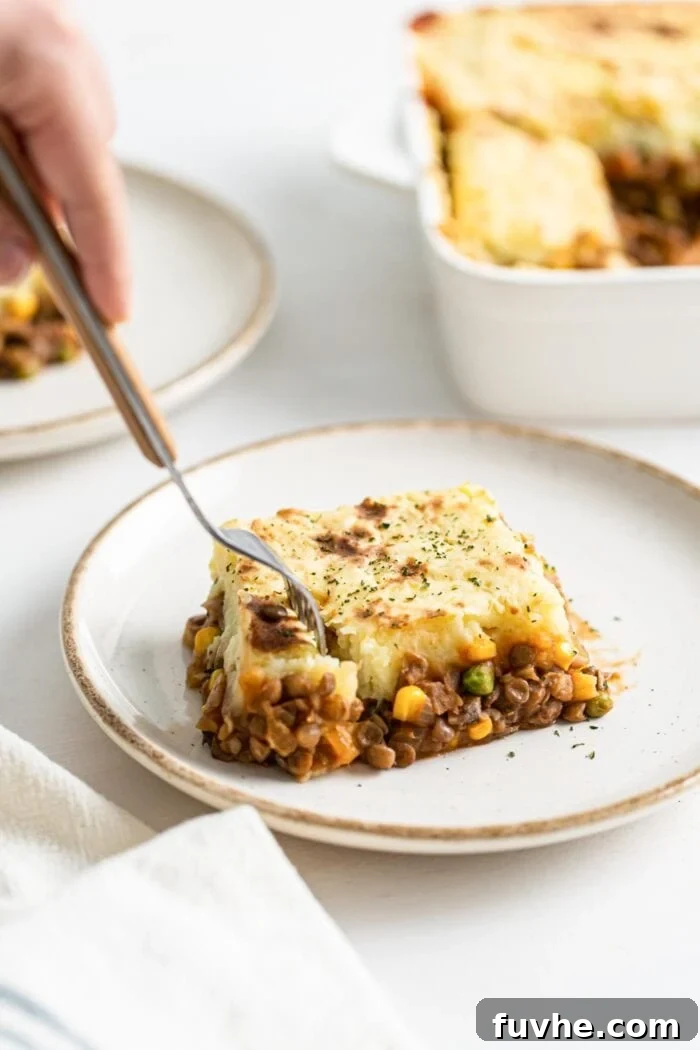 Comforting Vegan Lentil Shepherd's Pie 12 A fork lifts a small, perfect portion of vegan lentil shepherd's pie from a slice, showing the layers of creamy mashed potato and savory lentil filling.