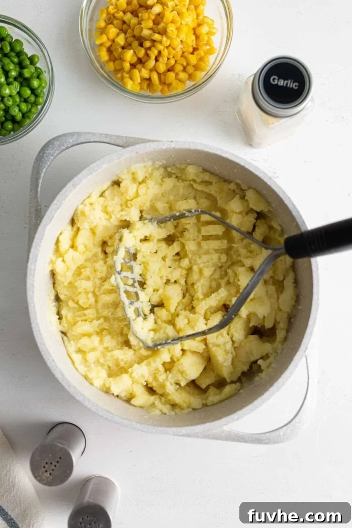 Comforting Vegan Lentil Shepherd's Pie 5 Creamy mashed yellow potatoes in a large pot, with a potato masher resting inside, ready to be spread.