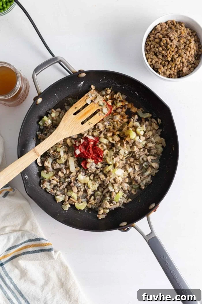 Comforting Vegan Lentil Shepherd's Pie 8 Onions, mushrooms, and garlic are simmering in a skillet, with a wooden spoon resting in the pan, ready to incorporate liquids.