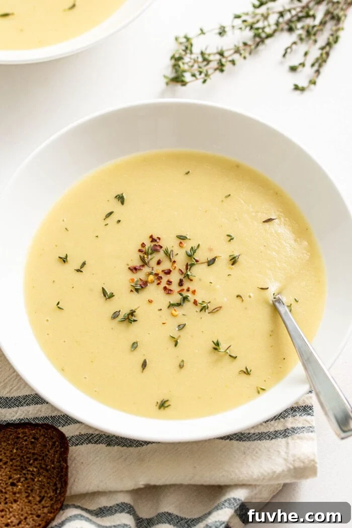 Creamy Vegan Potato Leek Soup 8 A beautifully presented bowl of creamy potato leek soup, elegantly topped with fresh rosemary sprigs and a sprinkle of red pepper flakes.