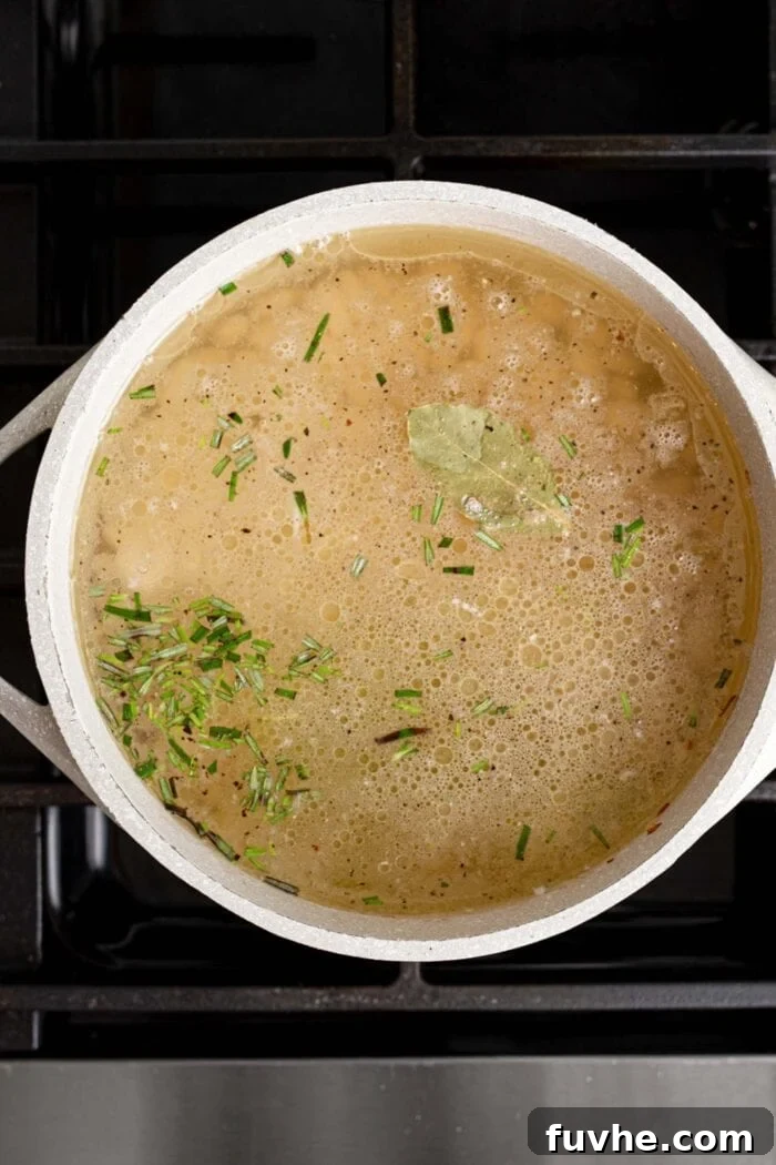 Nourishing Tuscan Kale and White Bean Soup 5 Brothy soup with rosemary cooking in a large pot on a gas range stovetop.