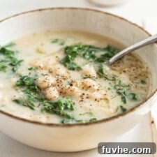 A bowl of creamy white bean kale soup with a spoon in it.