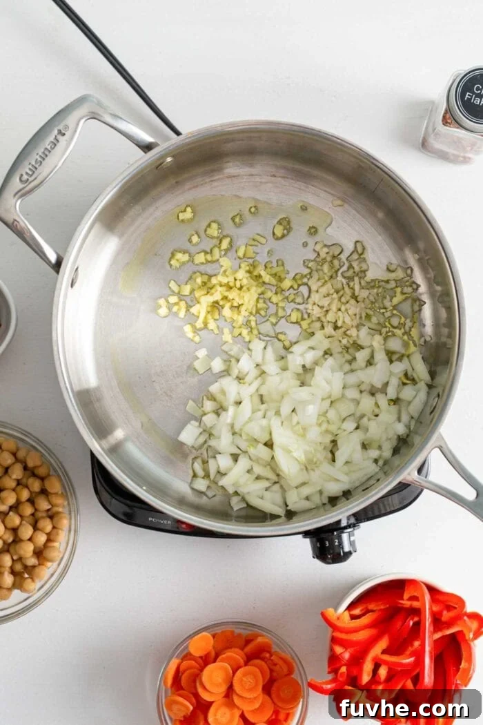 Onion, garlic and ginger cooking in a skillet on a small stovetop.