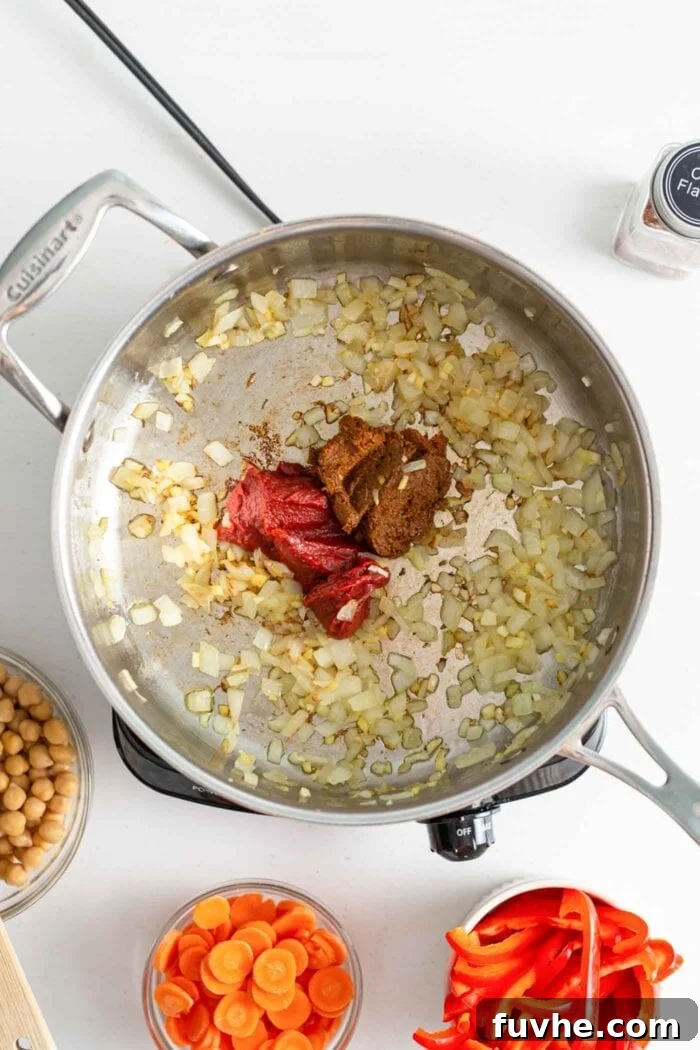 Curry paste and tomato paste added to a skillet of cooked onion, garlic and ginger.