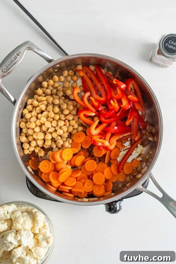 Chickpeas, chopped carrots and sliced bell peppers in a skillet cooking on a small stovetop.