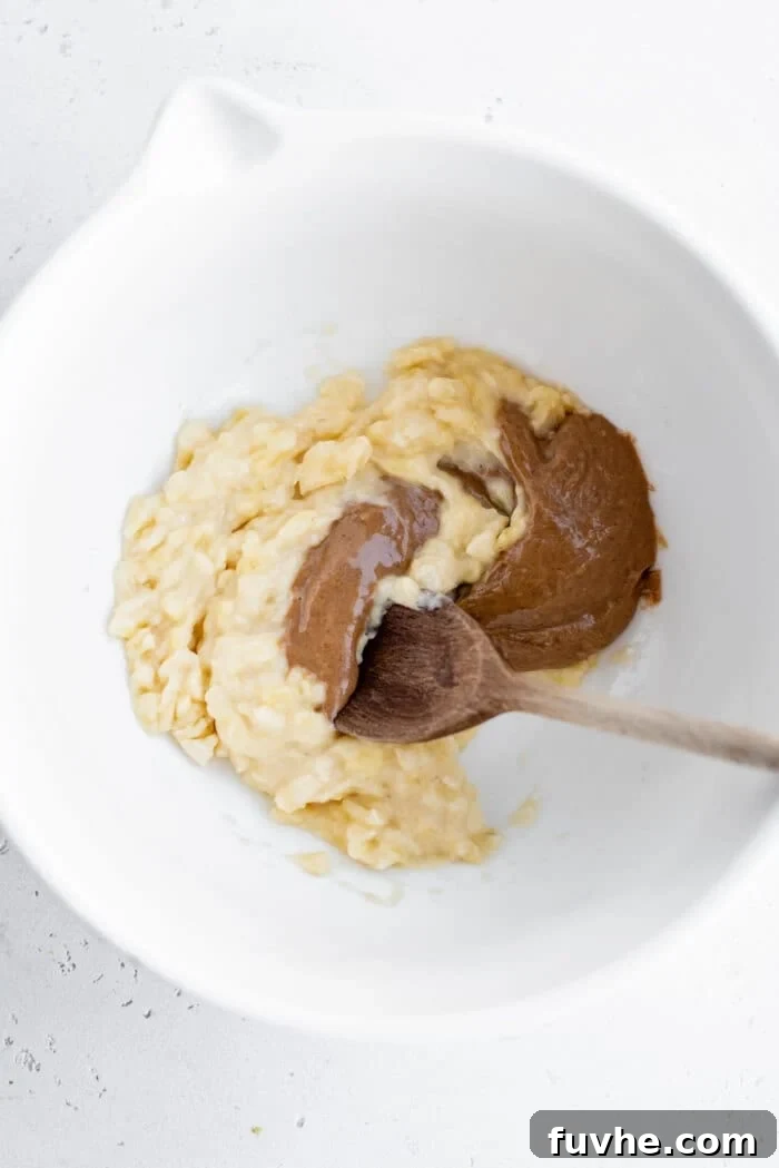 Mashed ripe banana combined with creamy almond butter and coconut sugar in a large mixing bowl, ready for the next wet ingredients.