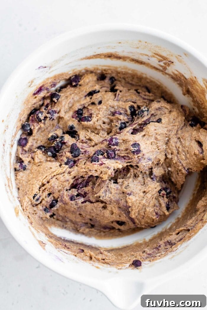 Raw blueberry muffin batter with visible blueberries gently folded in, ready for scooping into the muffin tin.