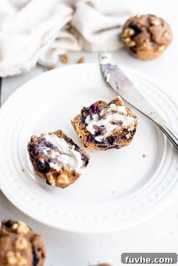A freshly baked vegan whole wheat blueberry muffin, sliced in half and spread with creamy vegan butter, ready to be eaten.
