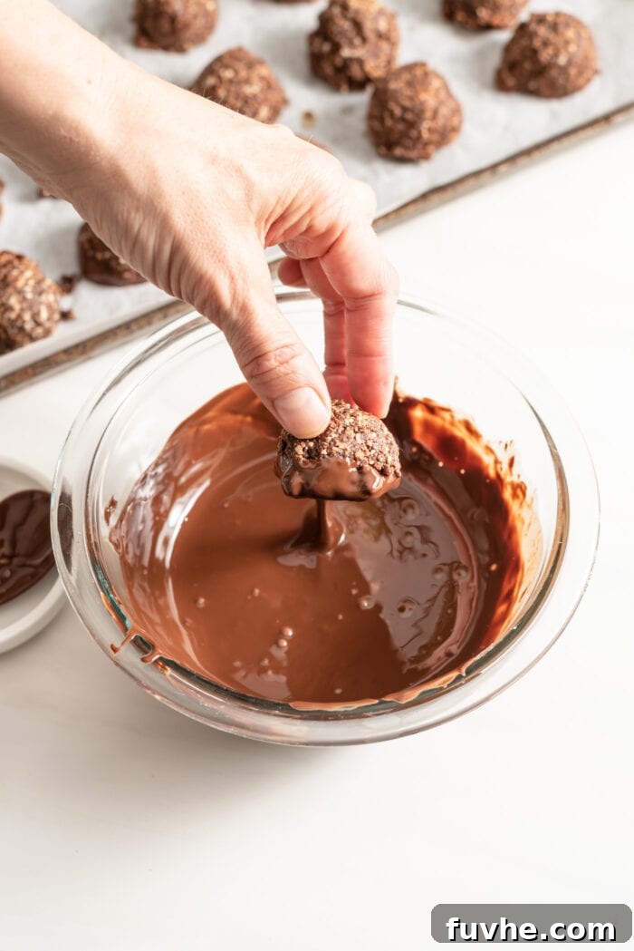 Decadent Vegan Chocolate Macarons 9 Hand dipping a macaroon into a bowl of melted chocolate.