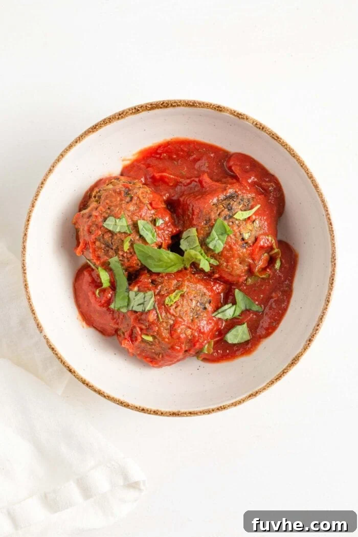 Savory Lentil Plantballs 11 An inviting overhead shot of three perfectly formed vegan lentil meatballs, elegantly served in a bowl, generously drizzled with vibrant tomato sauce and garnished with fresh basil leaves.