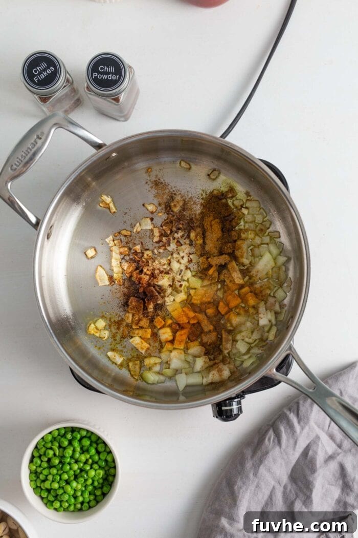Creamy Vegan Vegetable Korma 6 Aromatic mixture of sautéed onions, minced garlic, and ground spices including chili powder, ginger, cumin, turmeric, and curry powder, cooking in a skillet.