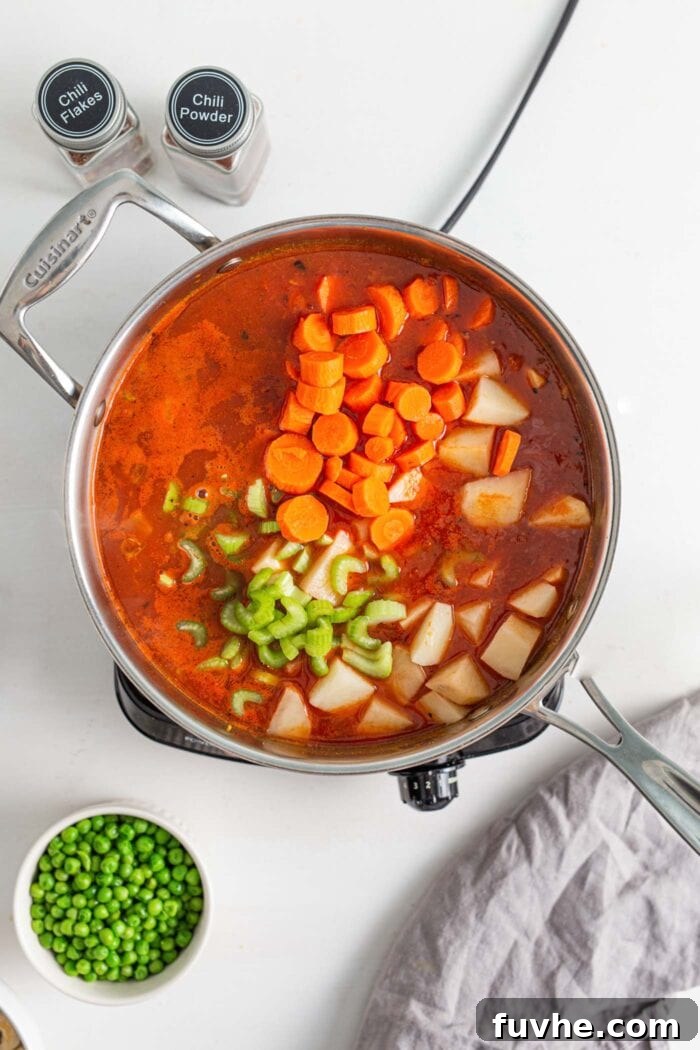 Creamy Vegan Vegetable Korma 7 A vibrant mix of crushed tomatoes, water, sliced carrots, diced potatoes, and chopped celery simmering gently in a large pot, developing rich flavors.