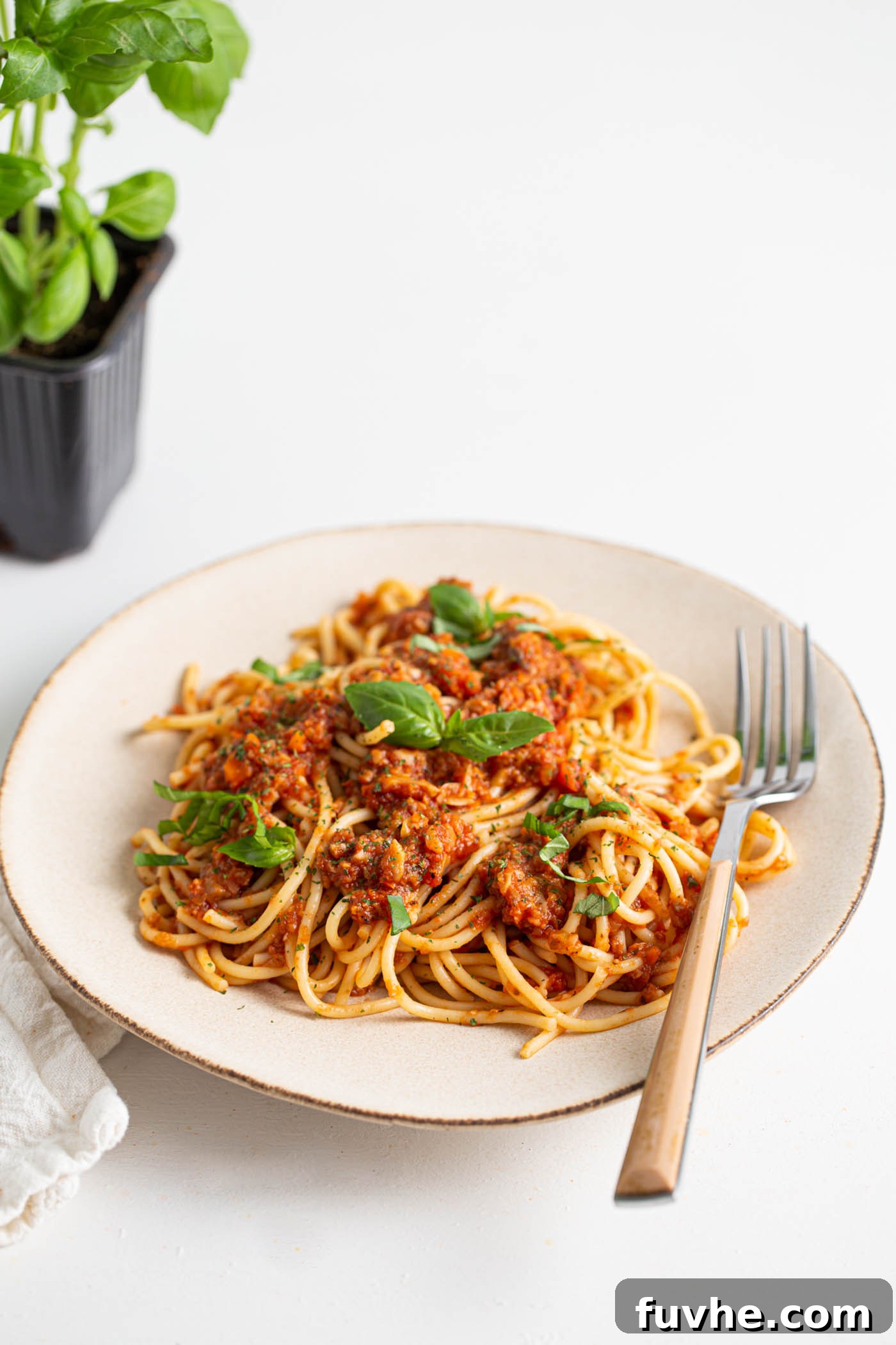 Hearty Vegan Mushroom Bolognese 2 Plate of vegan mushroom bolognese sauce over spaghetti topped with basil and parmesan. A fork rests on the plate and there's a fresh basil plant in the background.