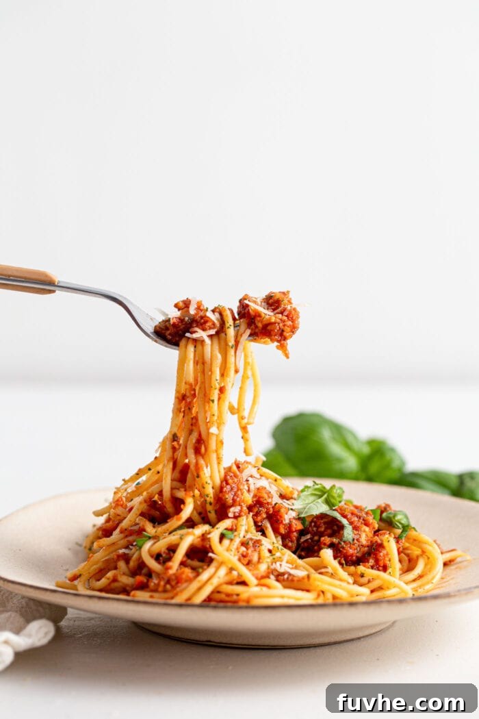Hearty Vegan Mushroom Bolognese 9 Fork lifting spaghetti and mushroom bolognese sauce topped with basil from a small plate.