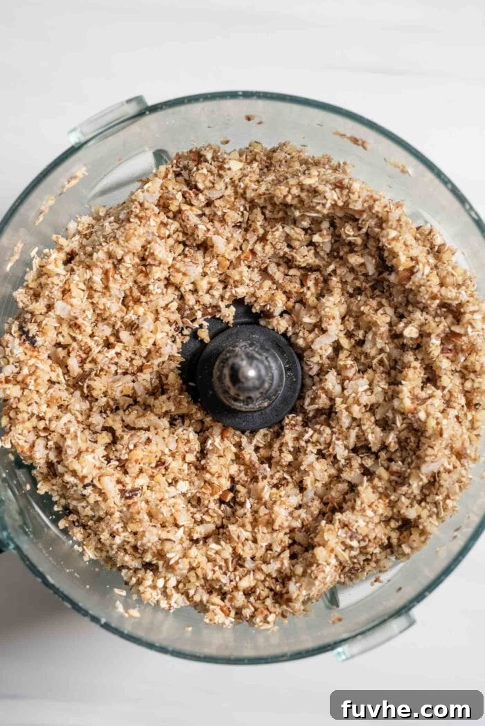 A mixture of blended oats, nuts, and brown rice in a food processor, showcasing its grainy yet cohesive texture.