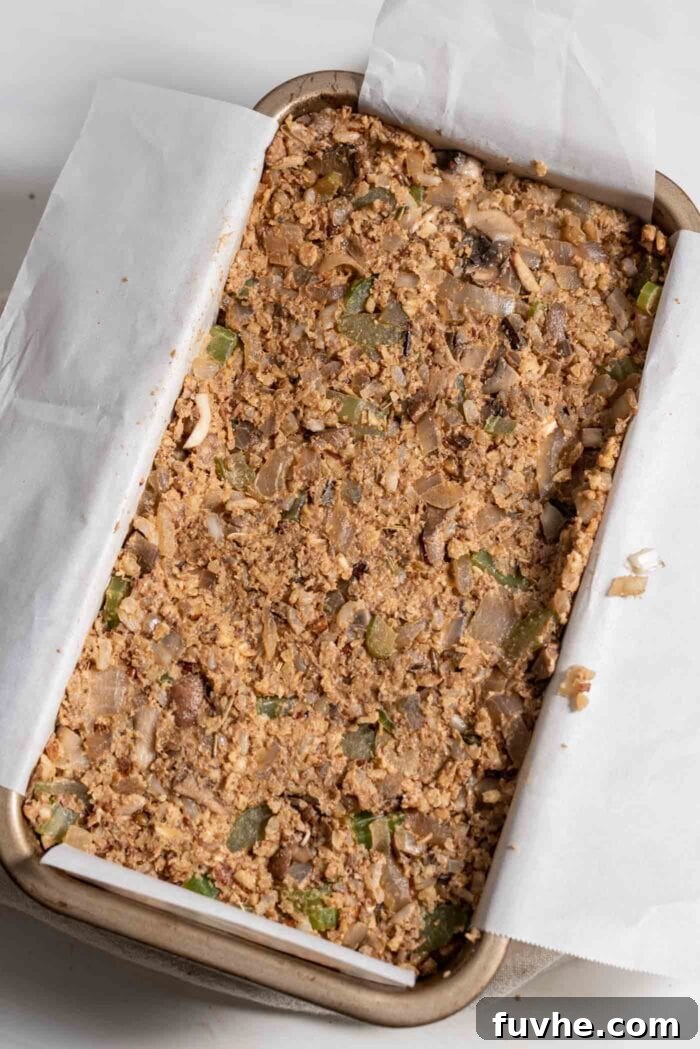 The unbaked nut roast mixture firmly pressed into a loaf pan, perfectly lined with parchment paper.