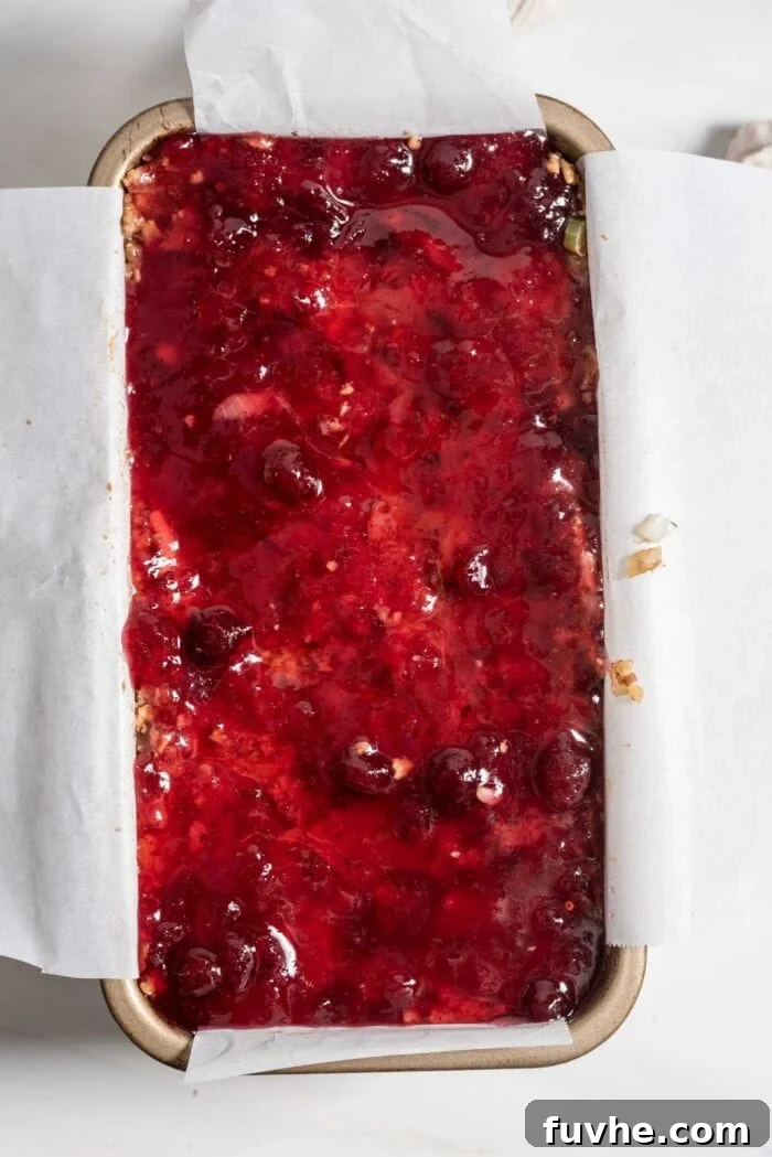 Vegan nut roast, artfully topped with a luscious whole berry cranberry sauce, nestled in a parchment-lined loaf pan, ready for baking.