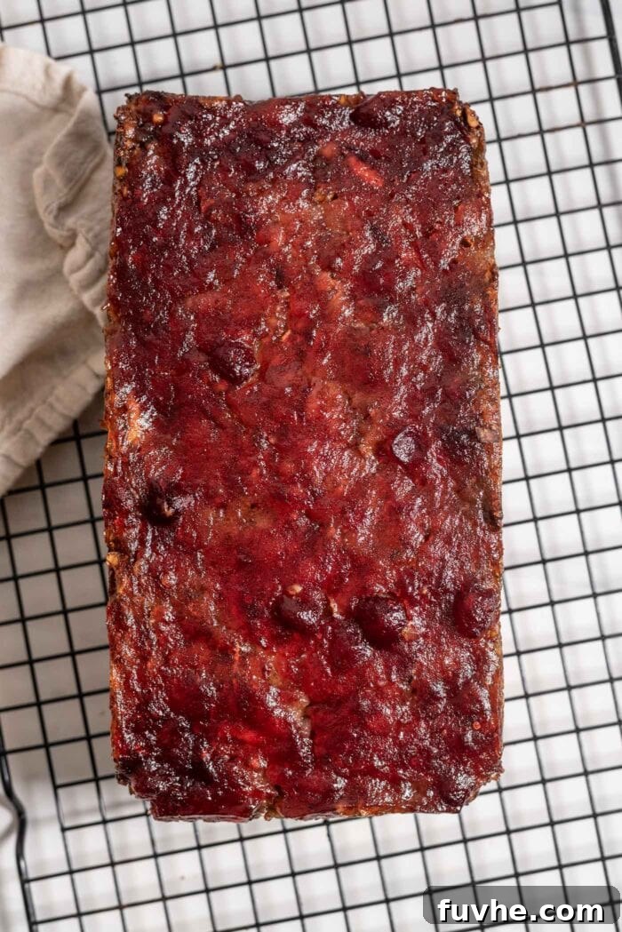 An overhead view of a beautifully baked vegan nut roast, topped with a shiny cranberry glaze, resting on a cooling rack.