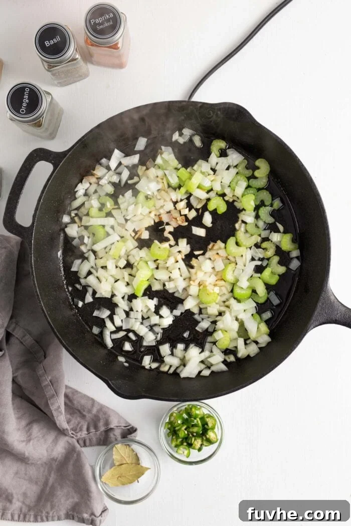 Onion, garlic, and celery cooking in a cast iron skillet, emitting steam and fragrance.