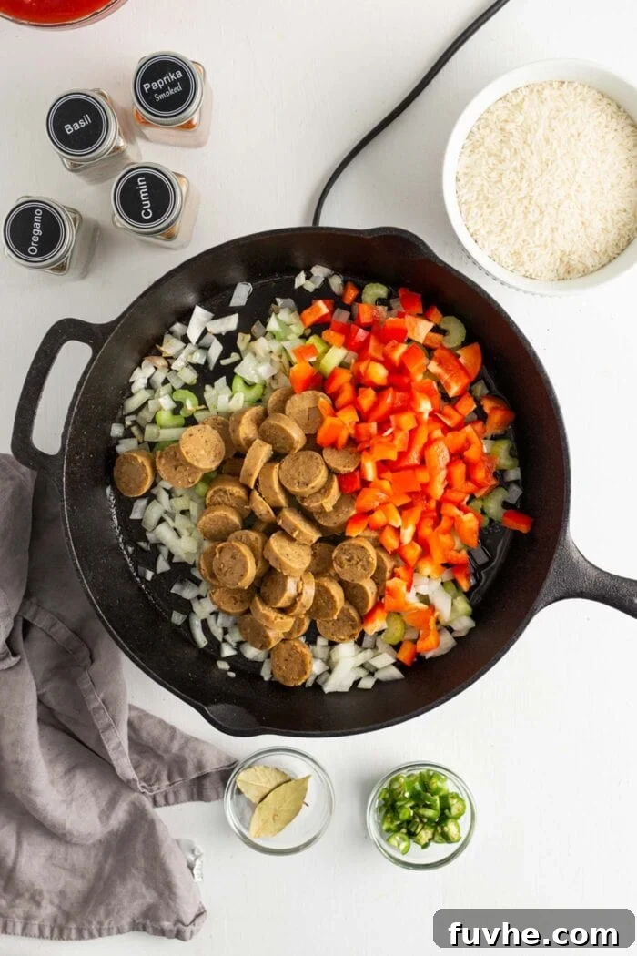 Sliced vegan sausage and colorful bell peppers added to a skillet with the sautéed onions, garlic, and celery.