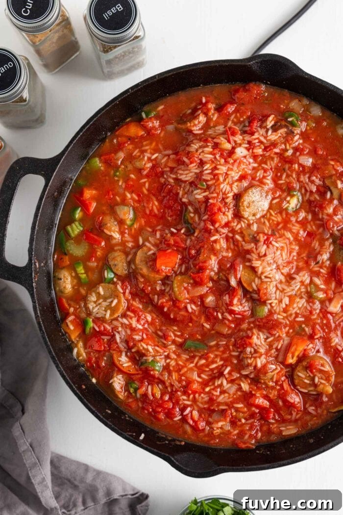 Tomato sauce, rice, and vegetables simmering in a skillet, ready for the oven.