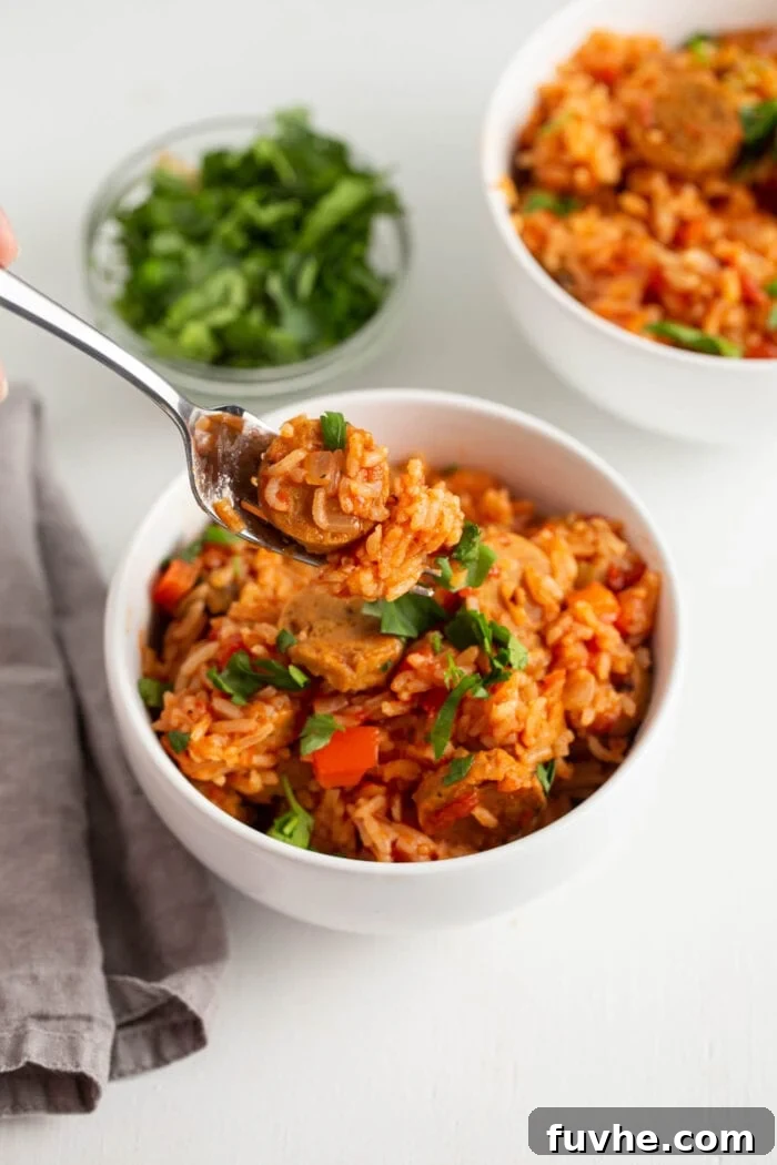 A forkful of delicious vegan jambalaya with a piece of plant-based sausage.