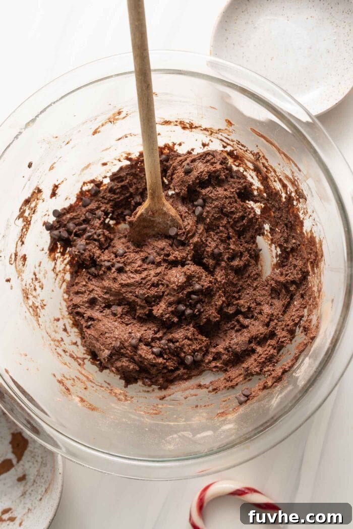 Irresistible Vegan Chocolate Peppermint Delights 5 Thick chocolate cookie batter studded with vegan chocolate chips in a mixing bowl.